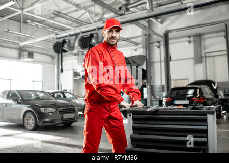 Two auto mechanics in red uniform walking with working cart at the car service Stock Photo