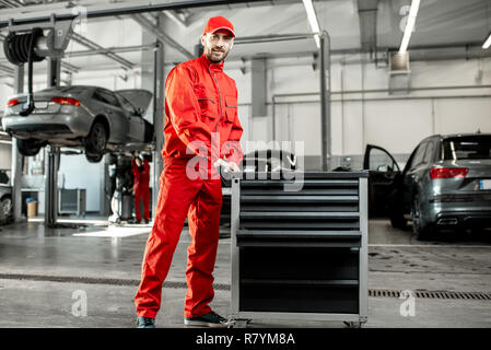 Two auto mechanics in red uniform walking with working cart at the car service Stock Photo