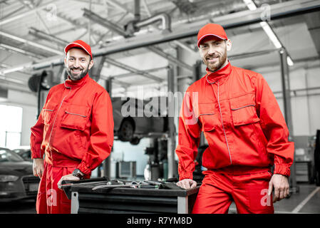 Portrait of a two handsome auto mechanics in red uniform standing with working tools at the car service Stock Photo