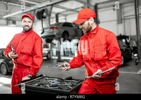 Portrait of a two handsome auto mechanics in red uniform standing with working tools at the car service Stock Photo