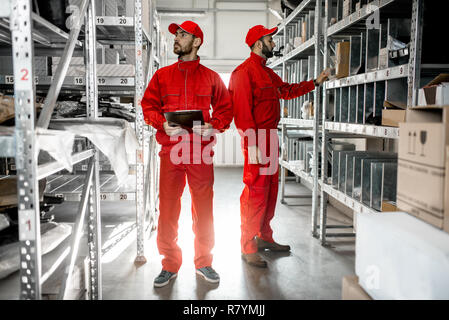 Warehouse workers in red uniform checking goods standing with clipboard in the storage with metal shelves Stock Photo