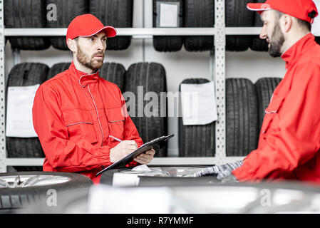 Two men in red uniform working in the warehouse with new car tires Stock Photo