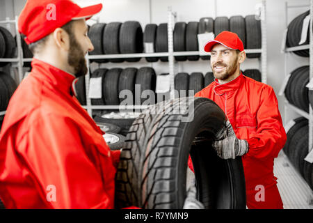 Two men in red uniform working in the warehouse with new car tires Stock Photo