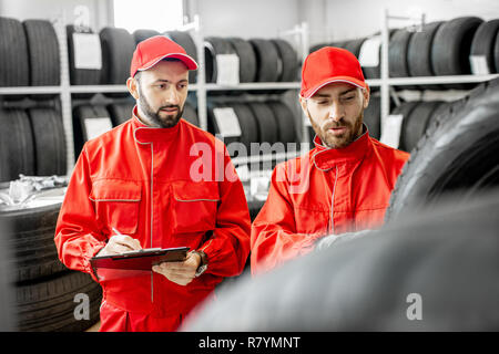 Two men in red uniform working in the warehouse with new car tires Stock Photo