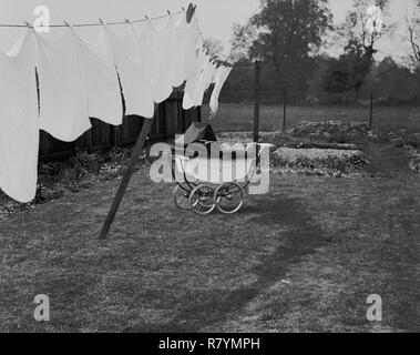 1960s, historical, washing hanging out on a clothes line to dry naturally in the fresh air and a traditional coach-built pram standing outside in a back garden, England, UK. Stock Photo