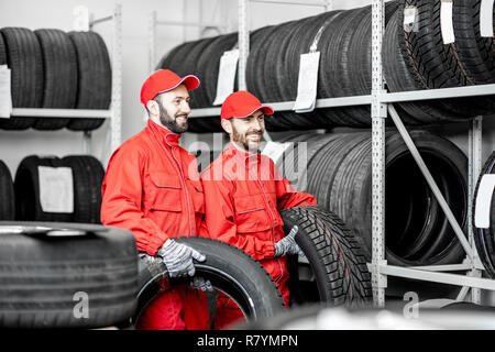 Two men in red uniform working in the warehouse with new car tires Stock Photo