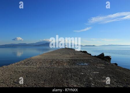 Beacon at the end of pier at Koronisia village in Ambracian gulf, Epirus Greece, calm blue sea, clouds in the sky Stock Photo