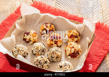 Set of handmade energy balls are lying in cardboard box on red napkin on wooden table. Stock Photo