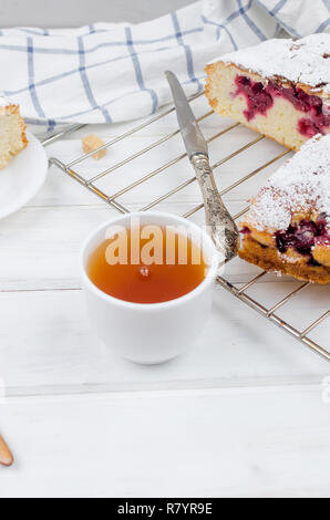 Cherry or plum pie sprinkled with icing sugar, cup of tea  on white wooden boards, close-up, view from above Stock Photo