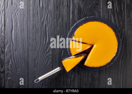delicious chocolate mango cheesecake cut in slices on a stone tray on a black wooden table with cake shovel, view from above, close-up, flatlay, copy  Stock Photo