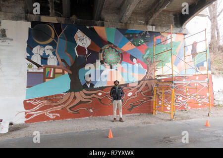 Artist Jordan Hamilton stands in front of his mural in progress under a bridge beside the Midtown Greenway bicycle Path. Minneapolis Minnesota MN USA Stock Photo
