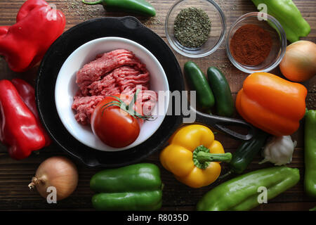 Raw ground beef inside skillet with peppers and other cooking ingredience around with wooden background top view Stock Photo