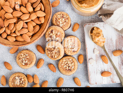 Homemade biscuit cookies with almond nuts and peanut butter on marble board on kitchen table background. Almonds in wooden bowl with jar and spoon of  Stock Photo