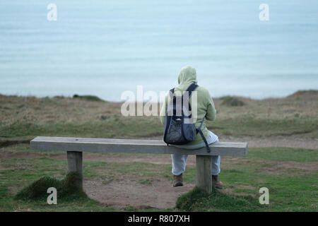 A figure sitting on a bench overlooking the sea in Porthtowan, ​Cornwall, UK. Stock Photo