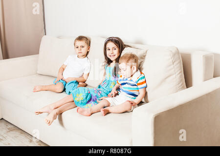 A photo of a beautiful little girl her two brothers sitting on the sofa. Stock Photo