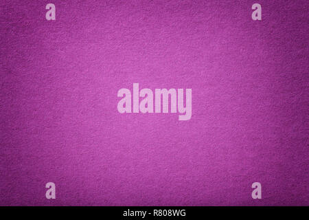 Dark purple matte background of suede fabric, closeup. Velvet texture of seamless magenta woolen felt with vignette. Stock Photo