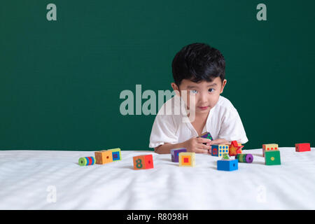 3 years old Asian boy play toy or square block puzzle on green chalkboard or school board background, kid lying learn by playing block shape or pieces Stock Photo