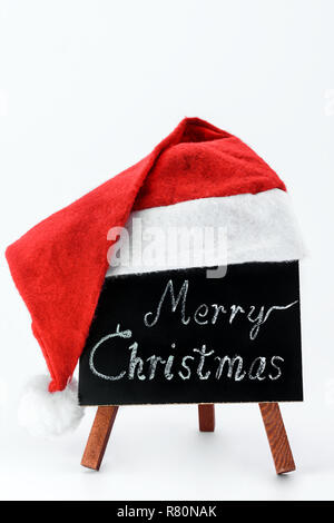 A blackboard with the text 'Merry Christmas' written in a chalk covered with a Santa Claus hat on a isolated white background. Stock Photo