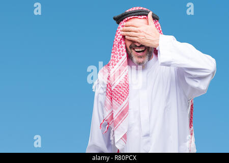 Senior arab man wearing keffiyeh over isolated background smiling and laughing with hand on face covering eyes for surprise. Blind concept. Stock Photo