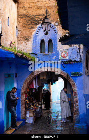 Morocco, Chefchaouen, Blue City, Medina, Al Kissariya, lane passing under arch in house containing shoe and clothing shop Stock Photo