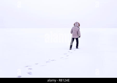Man walking on snow, footprints in snow, behind. Cold Siberian winter. Russia. The guy in the winter jacket with a hood. white down jacket Stock Photo