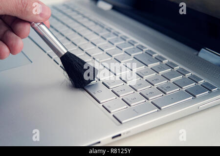 Cleaning and caring computer., cleaning the keyboard of the modern gray ultrabook transformer with a black brush from dust. Stock Photo