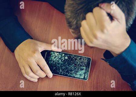 Desperate and astonished man holds cracked smartphone . Screen broken smartphone. Stock Photo