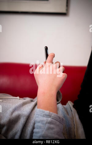 close up side view of a young man's hands holding a smartphone whilst lying on a red sofa in a domestic environment Stock Photo
