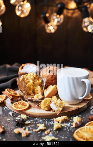 Traditional Christmas Panettone with raisins and dried fruits with hot milk or eggnog on wooden serving plate surrounded by crumbs on concrete table o Stock Photo