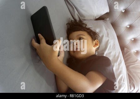 Asian thai kids lying on the bed and watching plays in the smartphone. Stock Photo