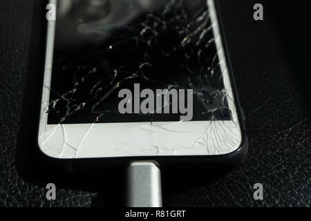 Close up of cracked smartphone screen lay on black leather. Stock Photo