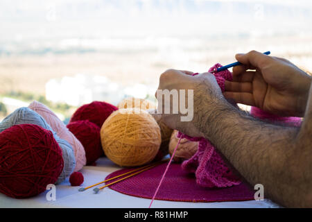a man knits a pink scarf for his daughter outdoors on a bright sunny day. Close up of a man's hairy hands. Woman's day. Stock Photo