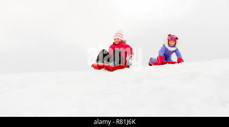 girls sliding on sleds down snow hill in winter Stock Photo