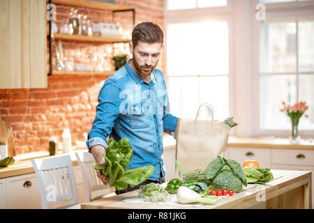 Handsome man in blue shirt unpacking healthy food from the shopping bag on the kitchen Stock Photo
