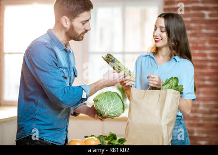 Young couple of vegetarians unpacking shopping back with fresh green product on the kitchen at home Stock Photo