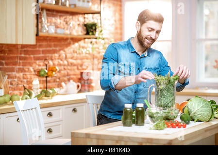 Handsome man filling blender with green raw food, making vegetarian smoothie on the kitchen at home Stock Photo