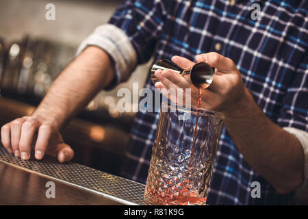 Young bartender standing at bar counter pouring whiskey into glass Stock Photo