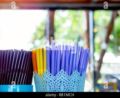 Colorful plastic straws, Purple, yellow, orange and brown in blue plastic container in coffee shop with copy space. Stock Photo