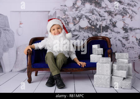 The boy opens Christmas presents from Santa Claus. Studio shot. In the background a white Christmas tree. Stock Photo