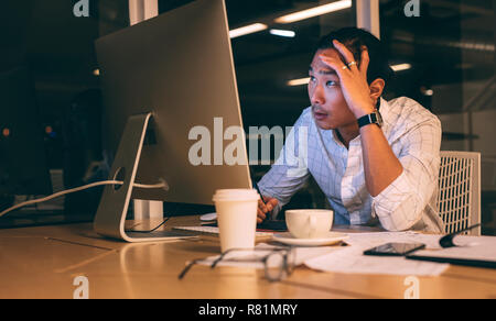 businessman sitting in front of computer with hand on head working late night. Entrepreneur looking tensed while working late in office. Stock Photo