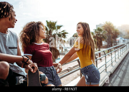 Beautiful woman standing by a railing outdoors with friends. Multiracial friends together outdoors with a skateboard. Stock Photo