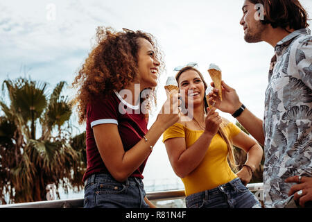 Smiling men and woman eating ice cream cone outdoors. Diverse group of friends eating ice-cream outdoors. Stock Photo