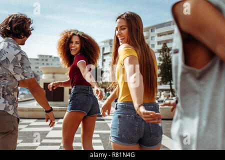 Smiling women and men walking and enjoying together outdoors.  Group of friends walking together on the street. Stock Photo