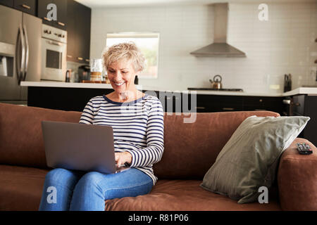 Senior white woman sitting on couch using laptop computer Stock Photo