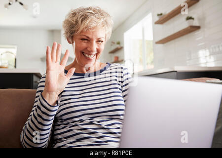 Senior woman video calling on a laptop, waving at screen Stock Photo