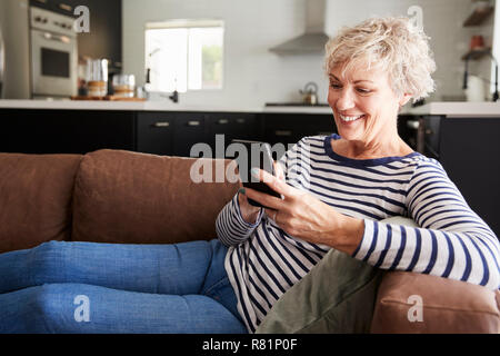 Senior white woman sitting on couch at home using smartphone Stock Photo