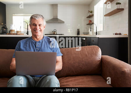 Senior white man sitting on sofa at home using laptop Stock Photo