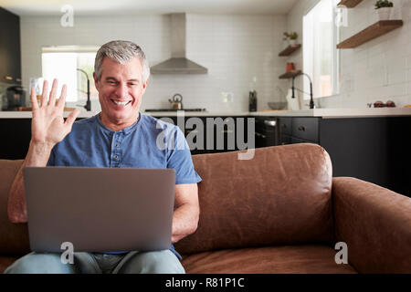 Senior man video calling on laptop at home, waving to screen Stock Photo