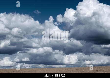 Impressive low hanging fluffy white clouds on a deep blue sky over a field of sand Stock Photo