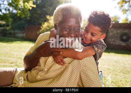 Senior black man sitting on grass, embraced by his grandson Stock Photo